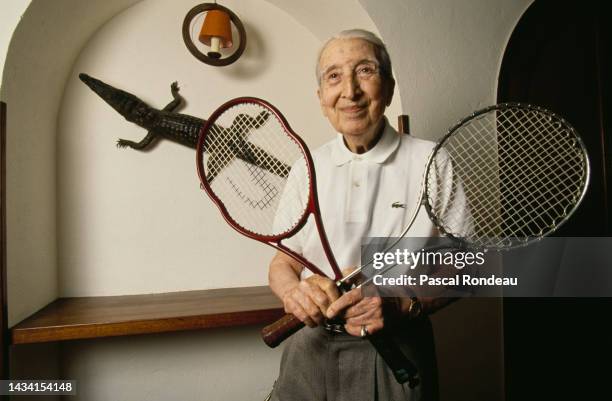 Portrait of French tennis player and fashion designer René Lacoste holding two tennis racquets, the Lacoste Equijet LT301 and a Wilson T2000 at his...