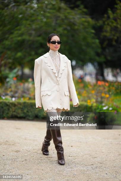 Aimee Song wears black sunglasses from Prada, white pearls earrings, a white lace print pattern high neck / long legging jumpsuit, a white linen...