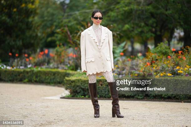 Aimee Song wears black sunglasses from Prada, white pearls earrings, a white lace print pattern high neck / long legging jumpsuit, a white linen...