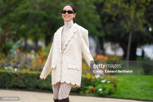 Aimee Song wears black sunglasses from Prada, white pearls earrings, a white lace print pattern high neck / long legging jumpsuit, a white linen...