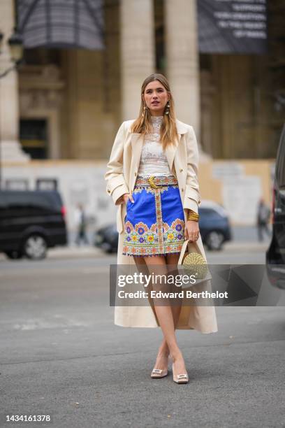 Zita D'Hauteville wears gold and white pearls pendant earrings, a white tulle with embroidered lace print pattern high neck blouse, a pale yellow...