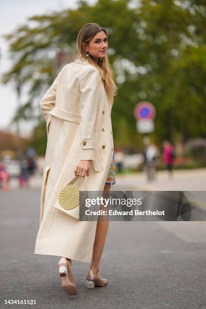 Zita D'Hauteville wears gold and white pearls pendant earrings, gold bracelets, a pale yellow matte leather handbag, beige shiny satin heels shoes...