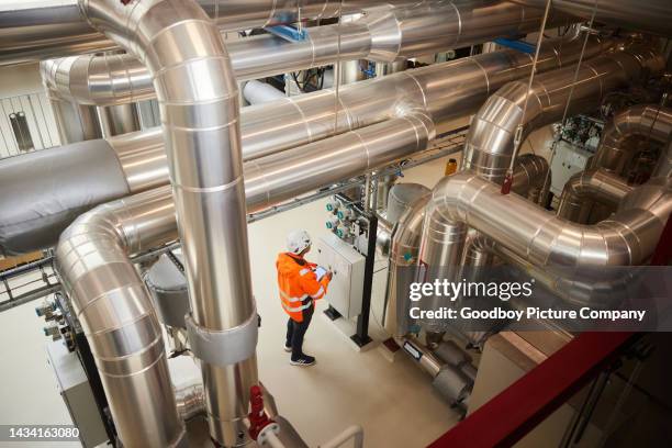 engineer standing with a tablet by a control panel in a power station - power station stock pictures, royalty-free photos & images