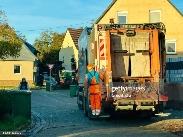 garbage worker continues with the garbage truck standing in his place at the back right - trailer trash stock pictures, royalty-free photos & images