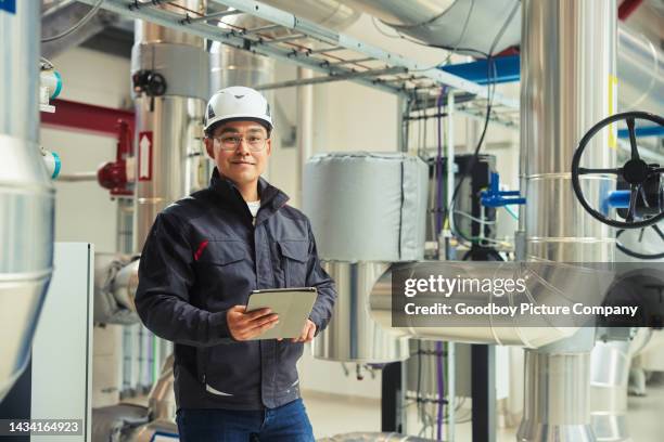 lächelnder junger ingenieur mit tablet in einem kraftwerk - heizungsmonteur stock-fotos und bilder