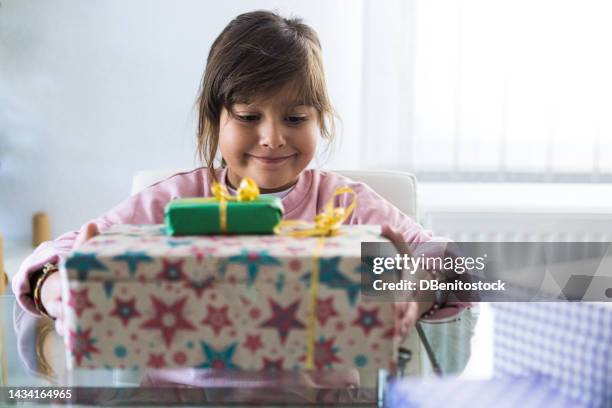 girl smiling in the living room of her house in the morning, opening gifts that have been given to her. concept of birthday, gifts, christmas holidays, emotion, magic and santa claus. - birthday gift stock pictures, royalty-free photos & images