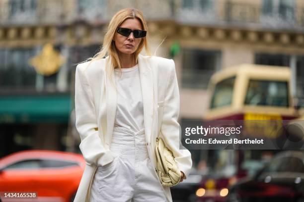 Elizabeth Sulcer wears black square sunglasses, a white t-shirt, a white latte shoulder-pads / oversized blazer jacket, high waist denim pants, a...