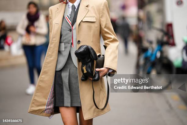 Kiwi Lee Han wears a white shirt, a gray tie from Thom Browne, a pale and dark gray pleated short skirt from Thom Browne, a beige long coat, a black...