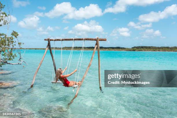drone view of young woman having fun on swing in a beautiful lagoon on a sunny day - mexico beach stock pictures, royalty-free photos & images