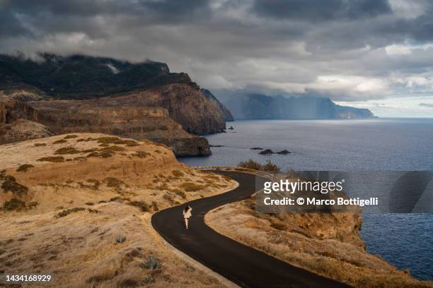 woman walking on a coastal road in madeira, portugal - madeira material stock-fotos und bilder