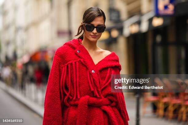 Gili Biegun wears black sunglasses, a red fluffy / sheep hoodie / oversized belted long coat, outside Stella McCartney, Paris Fashion Week -...