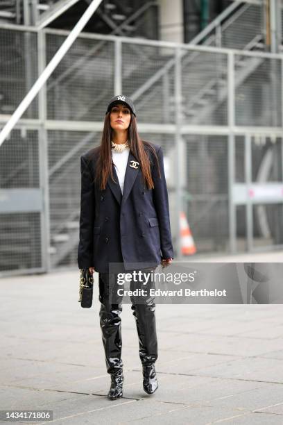 Elisa Taviti wears a black with embroidered white logo cap from New Era, a white pearls large necklace, a white t-shirt, a black oversized blazer...