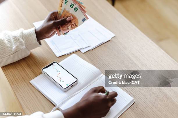 close-up shot of african-american woman holding european union currency, analyzing the financial graph - smartphone euro stockfoto's en -beelden