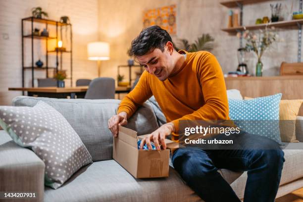 young man unboxing a package he ordered online - package imagens e fotografias de stock