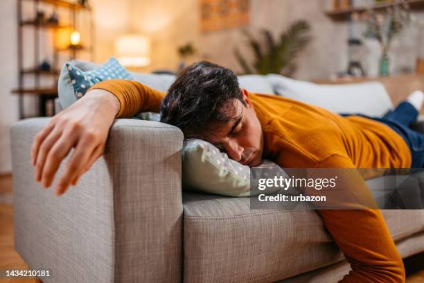 müder junger mann schläft auf dem sofa - auf dem bauch liegen stock-fotos und bilder