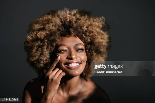 portrait of smiling woman applying moisturizer against a gray background - cream for face stock pictures, royalty-free photos & images