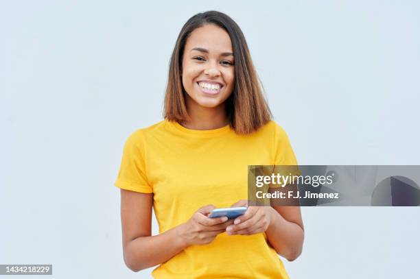 smiling woman using mobile phone in front of white wall - j lee fotografías e imágenes de stock