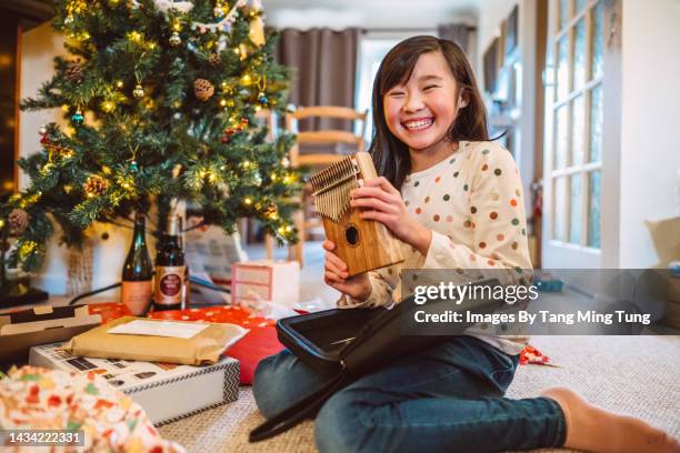 cheerful girl smiling joyfully at the camera with a thumb piano while opening her christmas presents at home on boxing day - boxing day tradition stock pictures, royalty-free photos & images