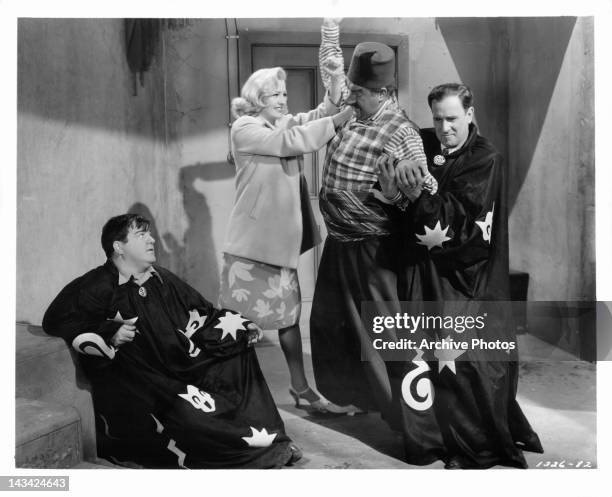 Lou Costello watches as Marilyn Maxwell and Bud Abbott wrestle unidentified man in a scene from the film 'Lost In A Harem', 1944.