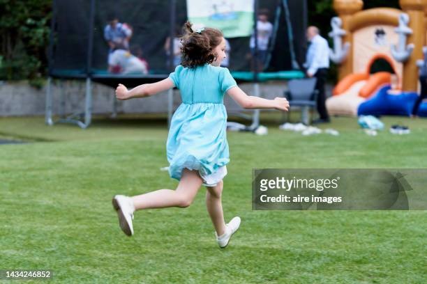 girl in blue dress running in an amusement park, back to camera, people with children in background - girl in blue dress stock pictures, royalty-free photos & images