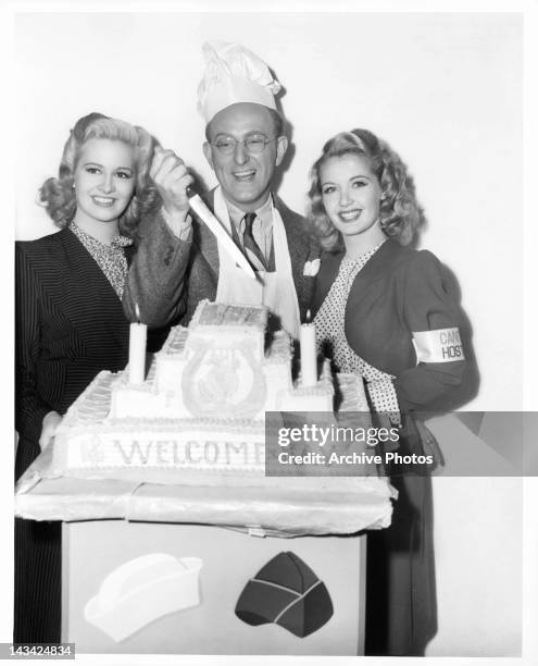 First day of shooting on his new picture, Kay Kyser is greeted with a four-tiered cake. Marilyn Maxwell and Mary Elliott are there for the first...