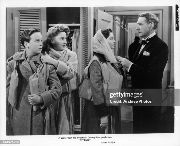 Barbara Stanwyck and Clifton Webb putting life vests on Audrey Dalton and boy in a scene from the film 'Titanic', 1953.