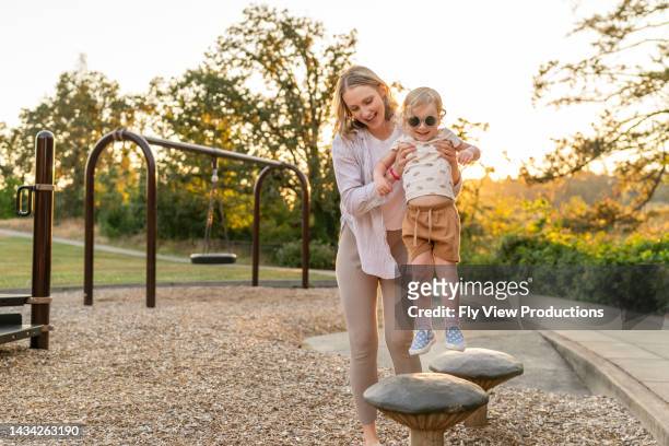mom and toddler daughter playing at the park - public park playground stock pictures, royalty-free photos & images