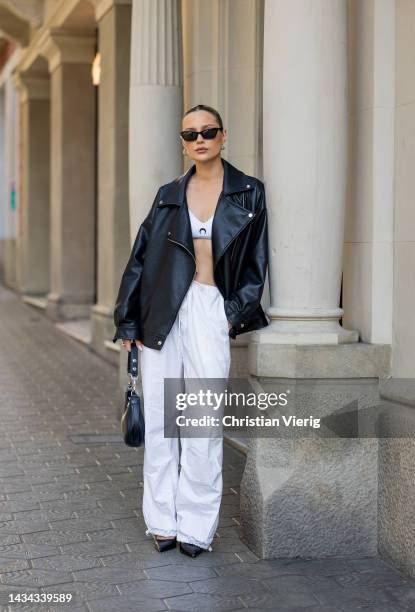 Nicole Böhm wears white pants, black Celine bag, black leather jacket, white Marine Serre cropped top, sunglasses, black pointed heels on October...