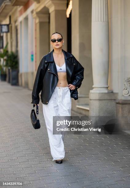 Nicole Böhm wears white pants, black Celine bag, black leather jacket, white Marine Serre cropped top, sunglasses, black pointed heels on October...