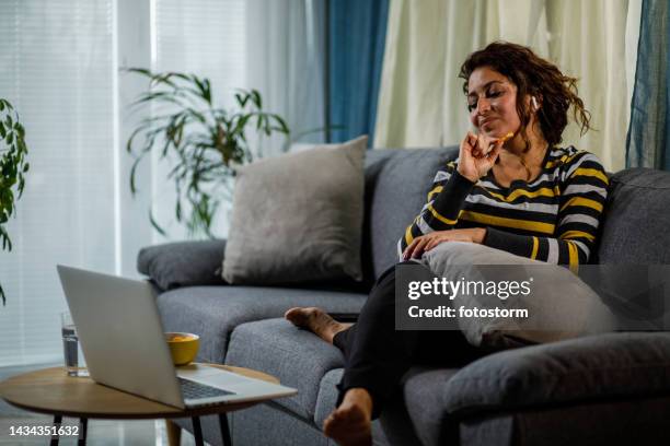 woman relaxing on the sofa and watching a movie on laptop - ecuadorian ethnicity stock pictures, royalty-free photos & images