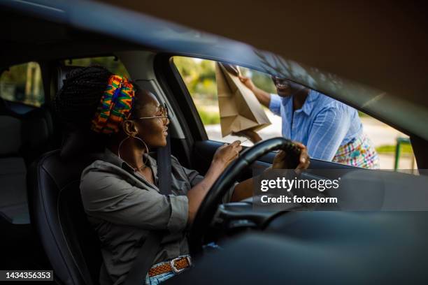 young woman receiving a paper bag with her takeaway order at the drive through - drive through stock pictures, royalty-free photos & images
