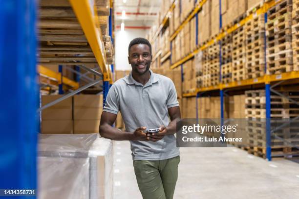 portrait of a male warehouse worker standing by rack with scanner device - cargo pants stock-fotos und bilder