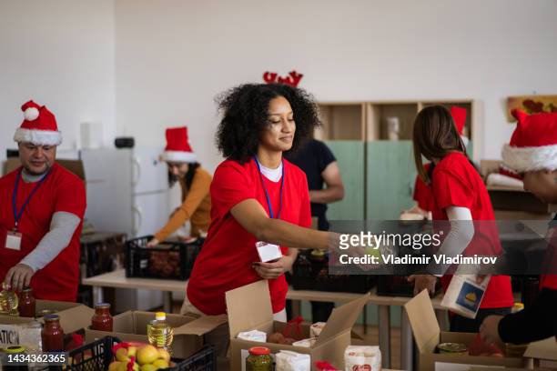 voluntarios festivos empacando comestibles en el banco de alimentos - evento de beneficencia fotografías e imágenes de stock