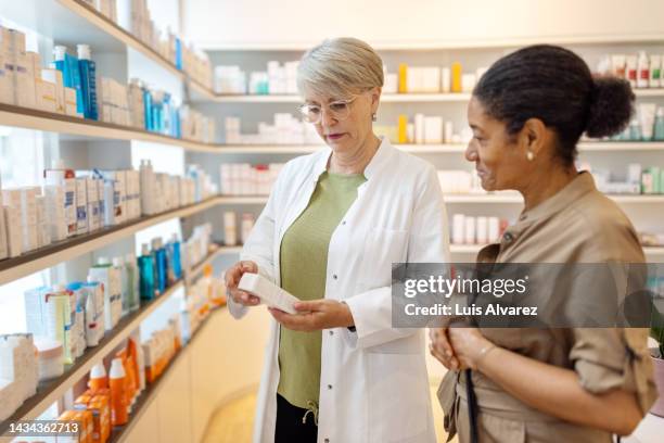 woman pharmacist assisting female customer at pharmacy - pharmacist explaining stock pictures, royalty-free photos & images