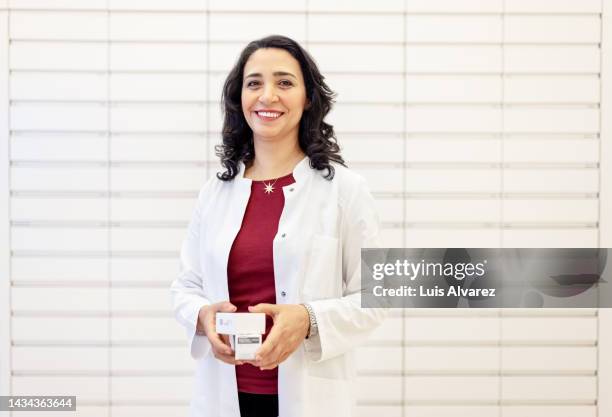 portrait of smiling woman pharmacist holding prescribed medicines in pharmacy storage room - pharmacist stock pictures, royalty-free photos & images