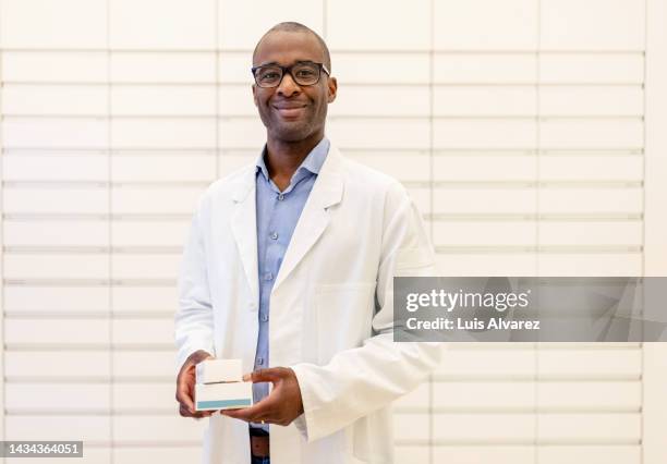 portrait of smiling african male pharmacist holding medicines in storage room - black pharmacist stock pictures, royalty-free photos & images