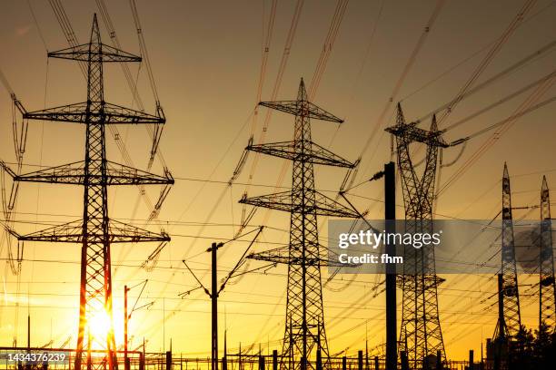 large electricity pylons at sunset - cable de energía eléctrica fotografías e imágenes de stock