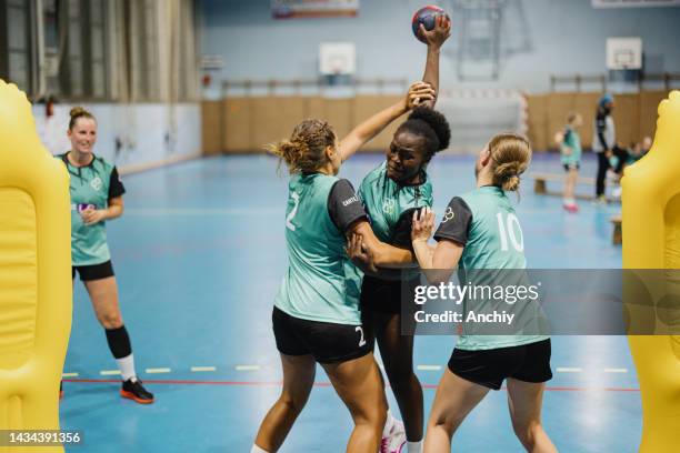 female handball player shooting at goal, while her teammates are trying to stop her - handbal stockfoto's en -beelden