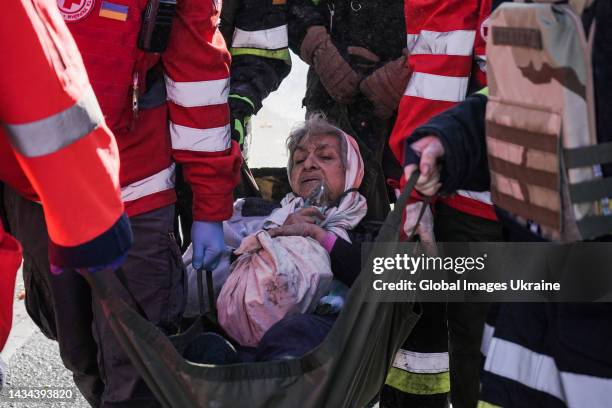 Rescuers carry a woman as she holds a bag with her surviving personal items at an area which was attacked by “kamikaze drones” on October 17, 2022 in...