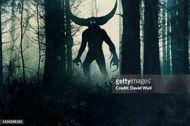 a horror demonic monster. with glowing eyes and horns. silhouetted in a dark, foggy winter forest. - monster fotografías e imágenes de stock