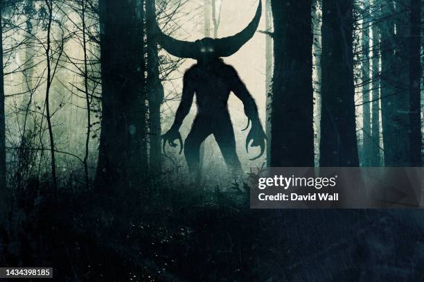 a horror demonic monster. with glowing eyes and horns. silhouetted in a dark, foggy winter forest. - demon foto e immagini stock