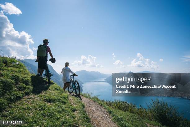 mountain biking couple push bikes up mountain ridge - gebirgskamm stock-fotos und bilder