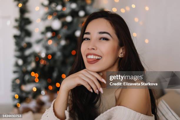 beauty portrait close-up of a beautiful multiracial asian positive young brunette woman smiling laughing and looking at the camera on a new year's holiday in a decorated room of the house in winter. joyful mixed race girl having fun on christmas vacation - winter skin stock pictures, royalty-free photos & images