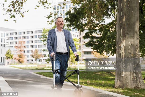 smiling senior man walking with mobility walker on footpath - rollator stock-fotos und bilder
