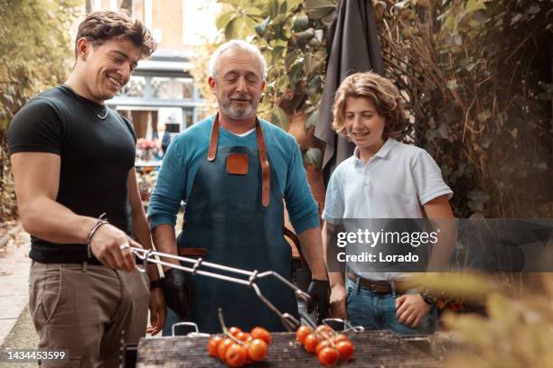 hübscher mann mittleren alters und seine familie bereiten bbq-essen auf einem außengrill zu - bbq tools stock-fotos und bilder