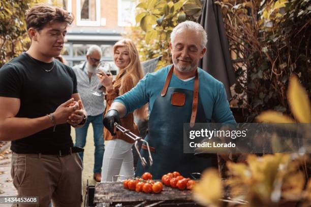 hübscher mann mittleren alters und seine familie bereiten bbq-essen auf einem außengrill zu - bbq tools stock-fotos und bilder