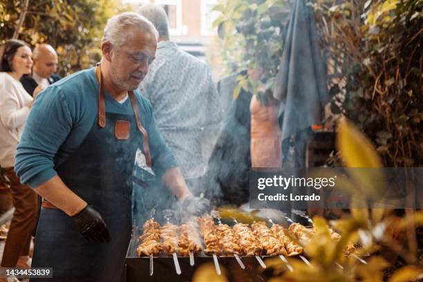 hübscher mann mittleren alters, der grillgut auf einem außengrill zubereitet - bbq tools stock-fotos und bilder