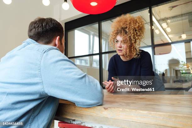 businessman and woman sitting at office table listening to each other - kommunikationsproblem stock-fotos und bilder