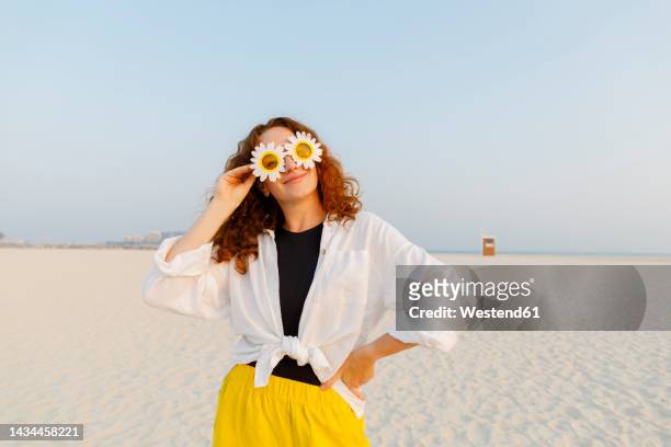 smiling woman wearing sunflower sunglasses standing with hand on hip at beach - happy sunflower stock pictures, royalty-free photos & images
