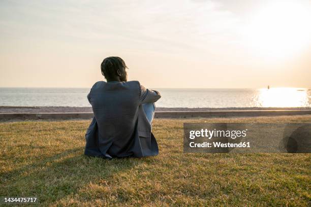 young businessman sitting on grass and admiring sea at sunset - man look sky stock pictures, royalty-free photos & images